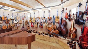 Una habitación con techo y paredes de madera, llena de diversos instrumentos de cuerda como violines, violonchelos y guitarras.