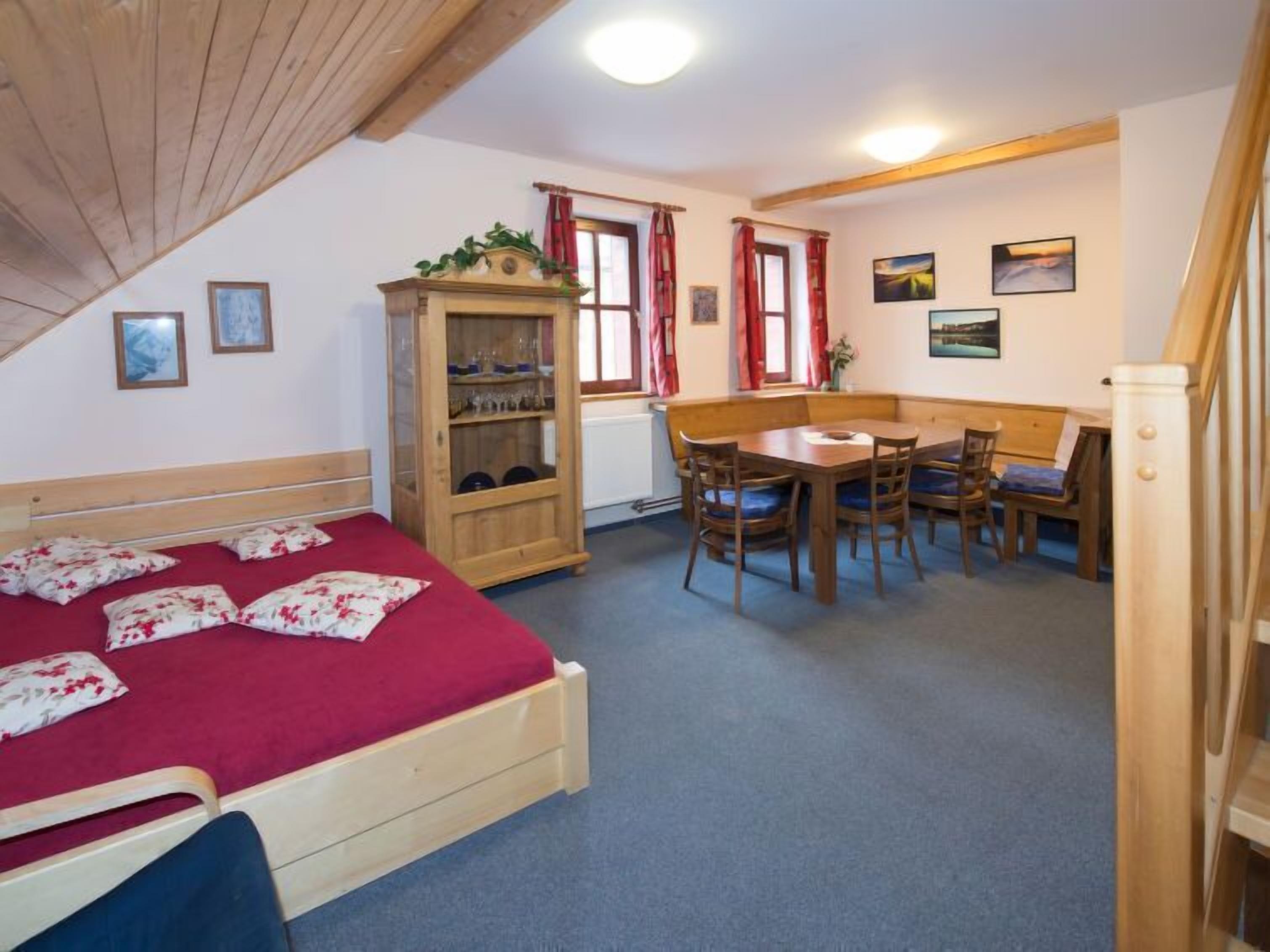 A bedroom with a wooden bed, a wooden cabinet, a dining table with chairs, and a red carpet.