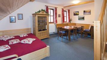 A bedroom with a wooden bed, a wooden cabinet, a dining table with chairs, and a red carpet.