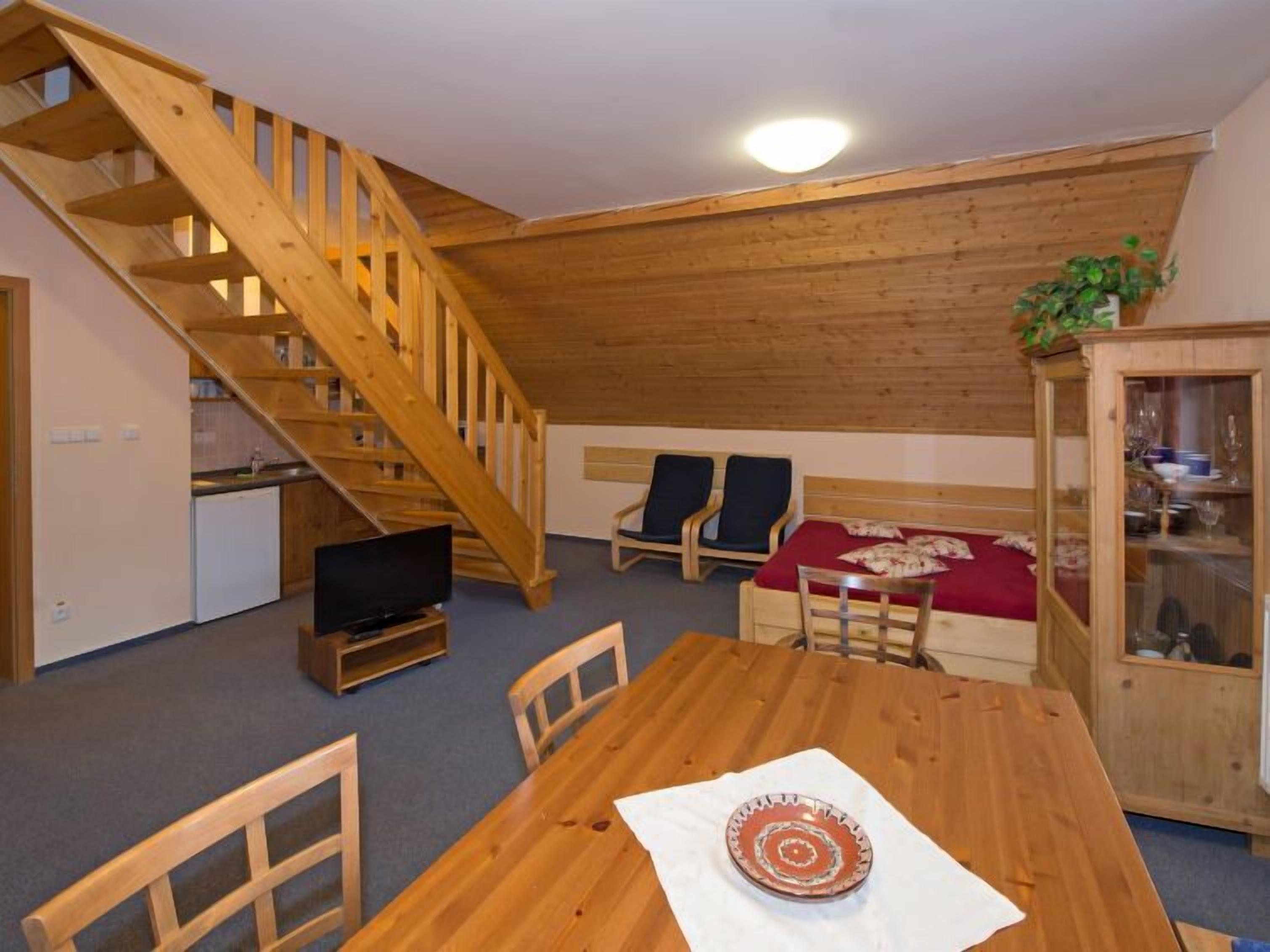 A cozy room with a wooden staircase, a dining table with chairs, a bed with a red blanket, and a small kitchenette.