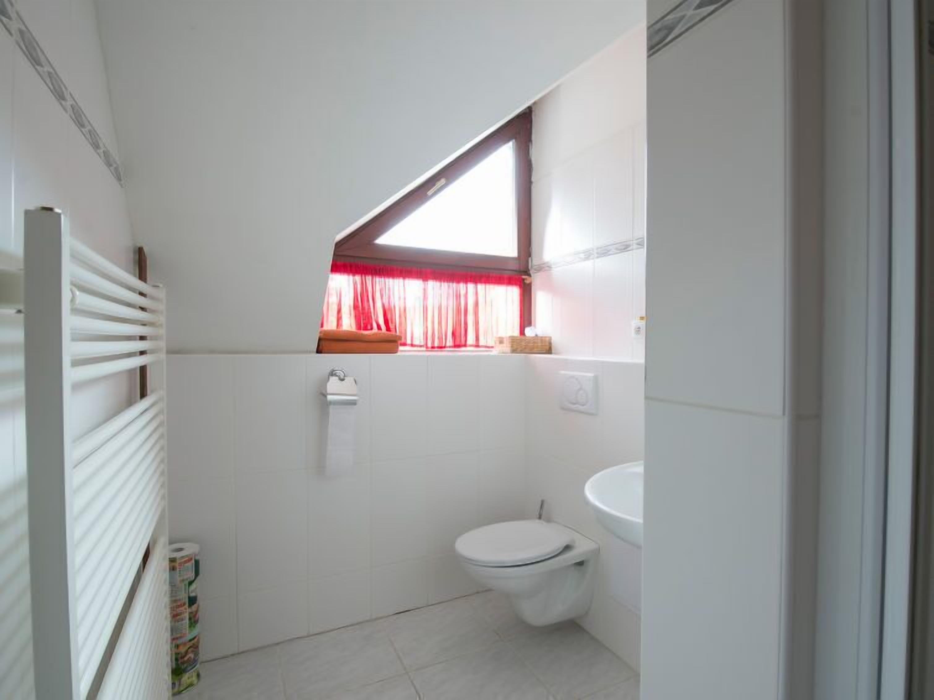 Een kleine, functionele badkamer met toilet, wastafel en een raam met rode gordijnen.