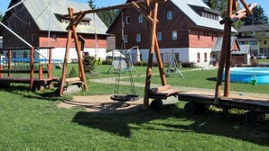 Un parque infantil con columpios y un tobogán en un área verde, con casas al fondo.