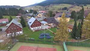 Una cancha de tenis con red, rodeada de edificios y un paisaje montañoso.