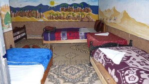 A room with three beds, a patterned rug, and a wall mural depicting a desert scene. - Hostel take your time 4228 (Zagora)