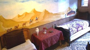 A hotel room with a large desert-themed mural on the wall, a bed, a small table with a vase of flowers, and a patterned rug. - Hostel take your time 4228 (Zagora)