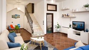 Un salon avec un escalier, un coin repas avec des chaises colorées, un téléviseur et une plante.