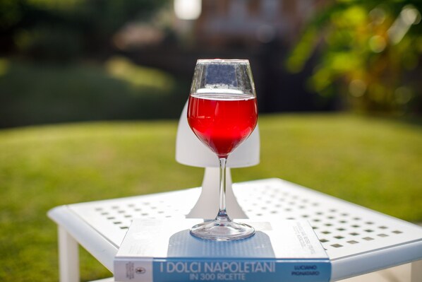 A wine glass with red liquid on a white table with a book titled "I dolci napoletani in 300 ricette" by Luciano Ponzio.