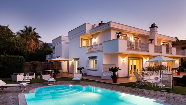 Une maison à deux étages avec une piscine, un espace salon extérieur et un balcon bien éclairé.