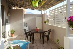 A covered patio with a table and chairs, potted plants, and a white railing.