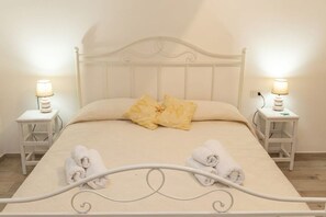 A neatly made bed with two pillows, two bedside tables with lamps, and two rolled towels on the bed.