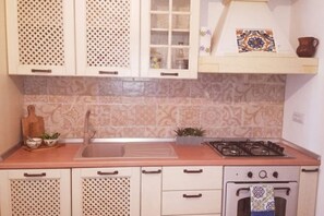 A kitchen with patterned tiles, a sink, cabinets with handles, a stove, and a decorative tile above the stove.