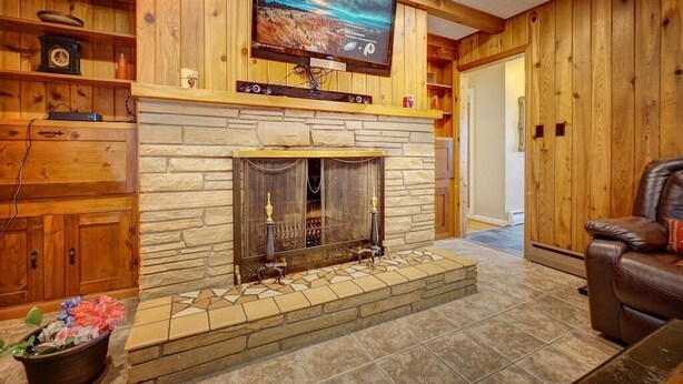Una sala de estar con chimenea de piedra, paredes de madera, televisor montado y sofá de cuero.