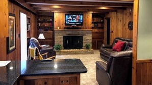 Una sala de estar acogedora con chimenea de piedra, sofás de cuero, televisor de pantalla plana y paneles de madera.