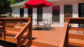 Una terraza de madera con un paraguas rojo, una mesa y sillas.