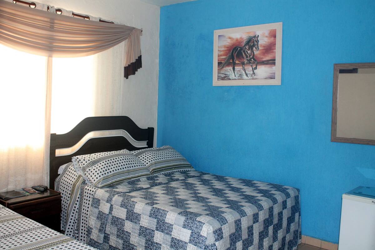 Ein Schlafzimmer mit einem Bett, einem Nachttisch, einem Wandbild und einem Fenster mit Vorhängen.