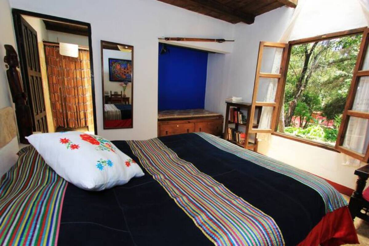 A bedroom with a bed, a window with a view of greenery, a mirror, and a blue wall.