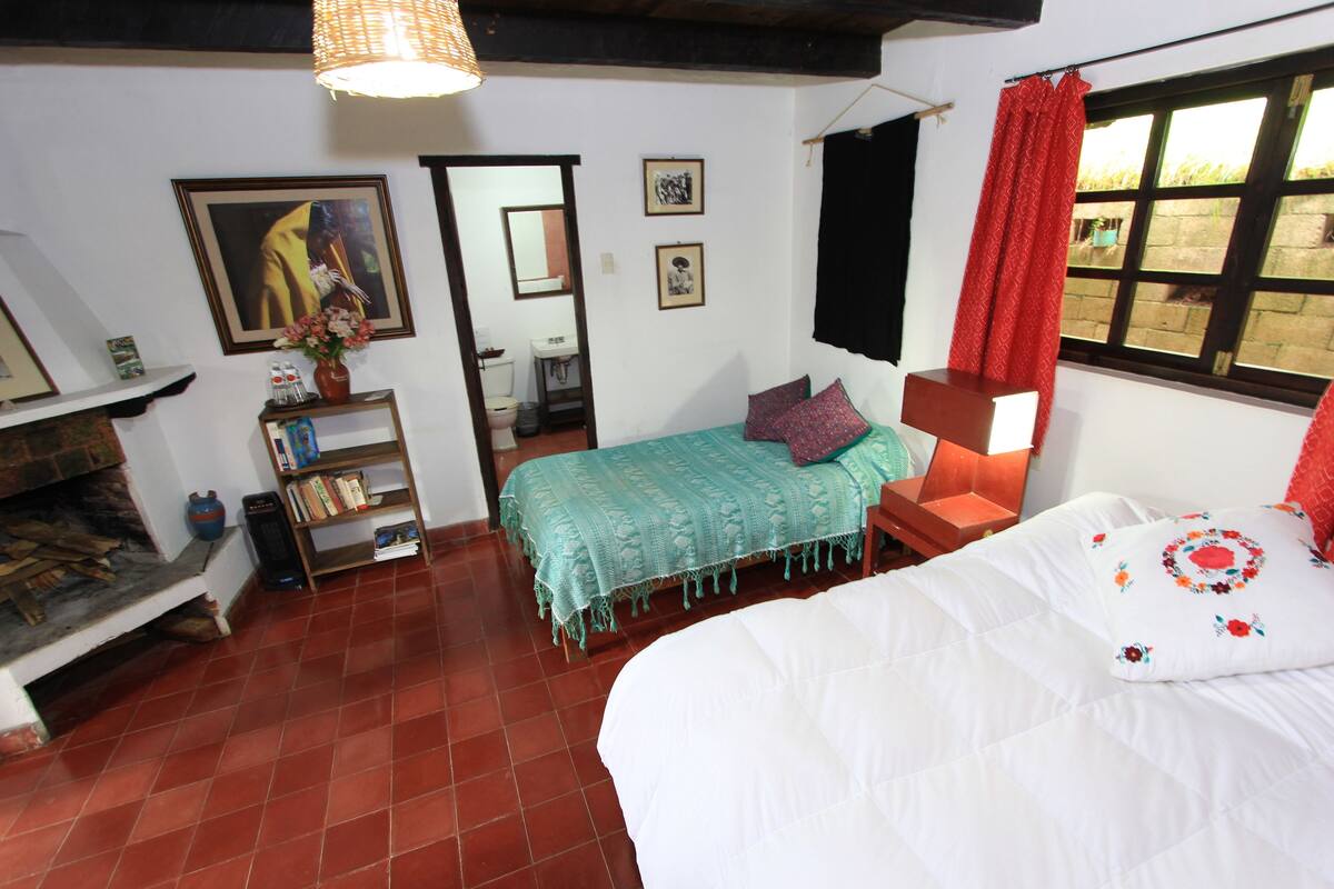 A bedroom with a bed, a bookshelf, a mirror, and a window with red curtains.