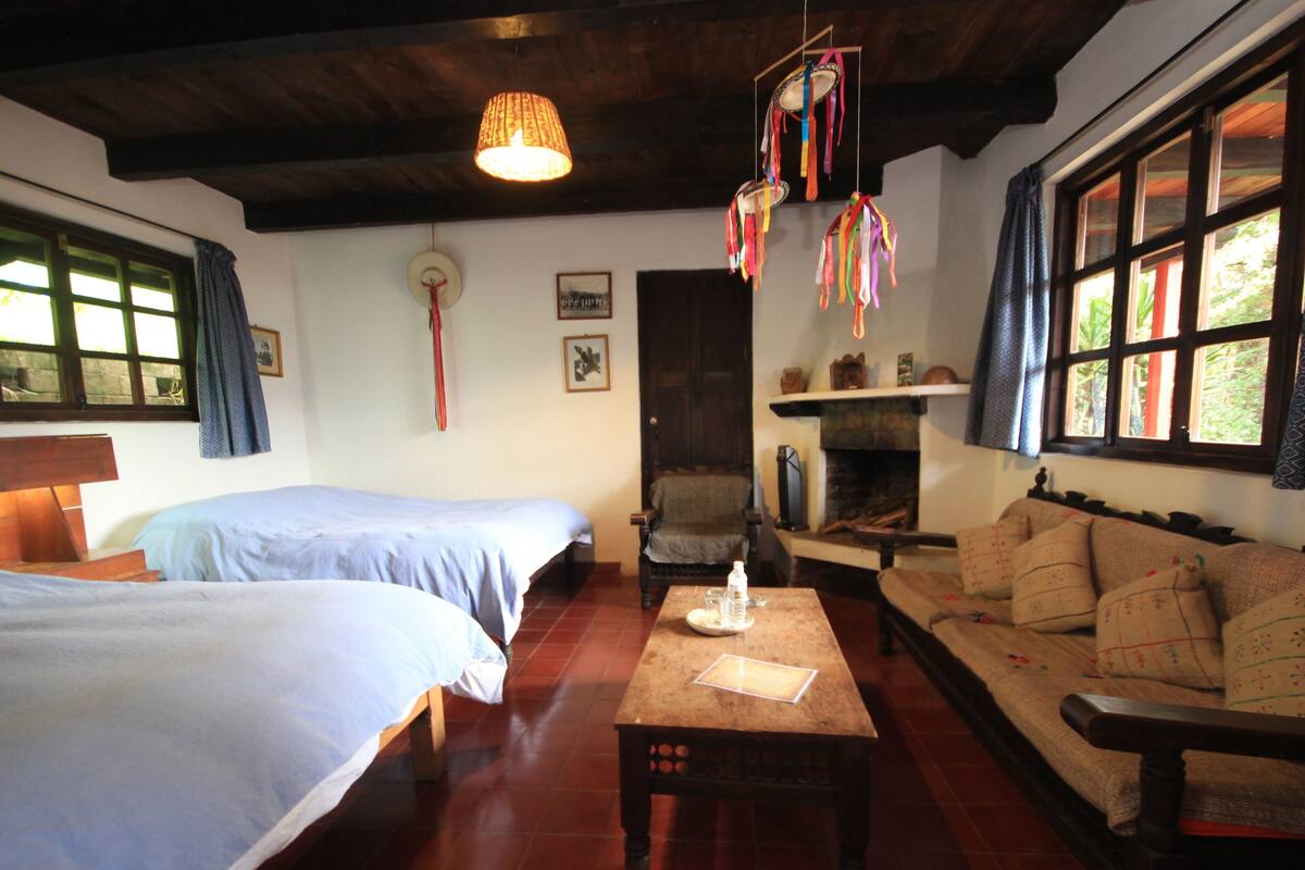 A cozy room with two beds, a sofa, a wooden table, and a hanging decoration.