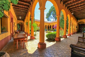 An open courtyard with a wooden table and chairs, surrounded by yellow columns and arches, and a sign reading "RESTAURANTE." - Hotel Na Bolom (San Cristóbal de las Casas)