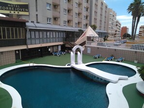 A swimming pool with a unique design, surrounded by lounge chairs and a hotel named "Hotel Torrejoven". - Hotel Torrejoven (Torrevieja)