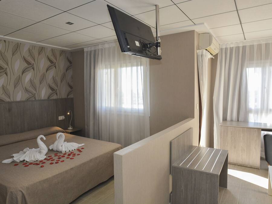 Une chambre d’hôtel avec un lit, un bureau, une télévision et une fenêtre avec des rideaux.