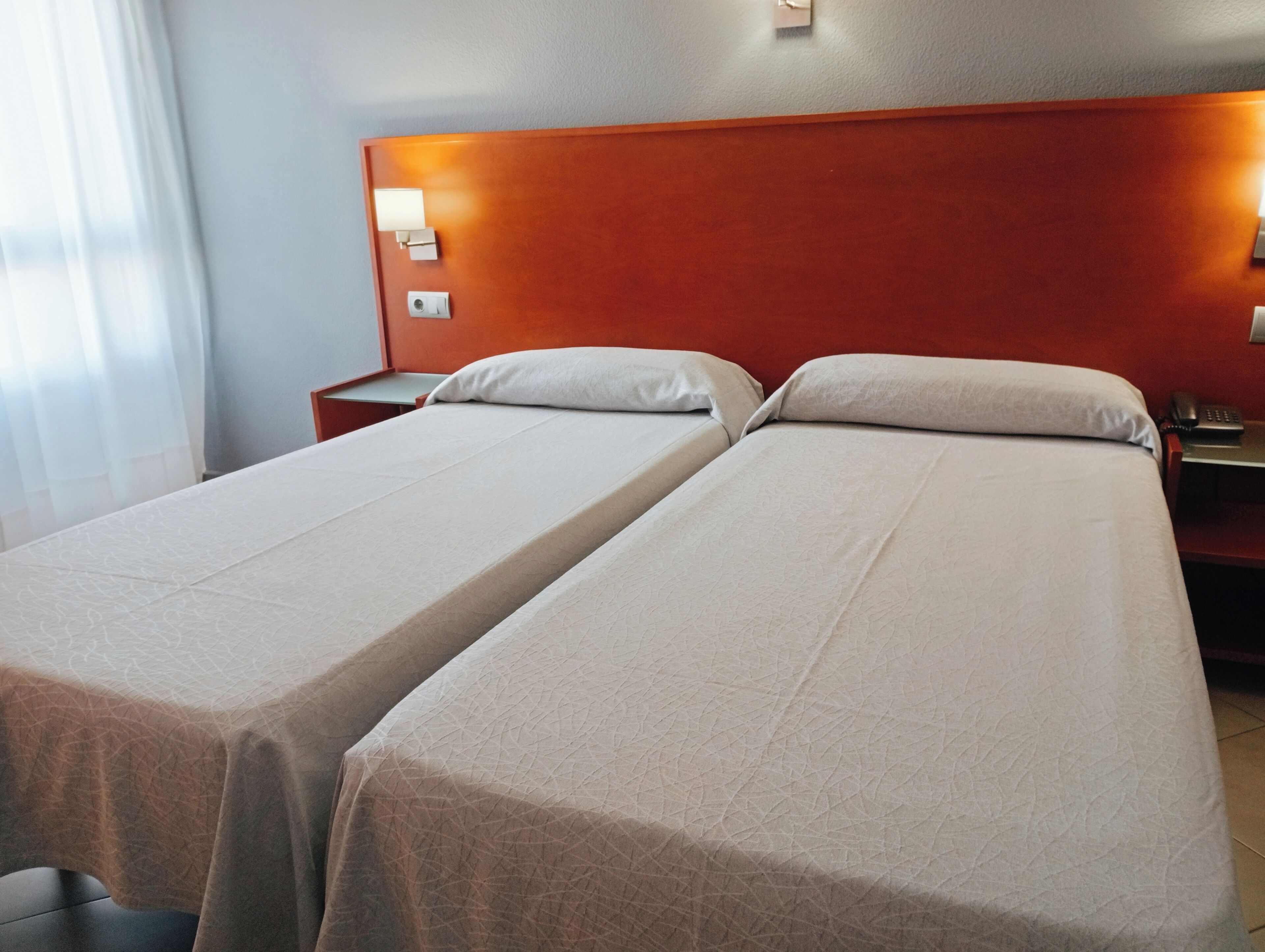 Une chambre d’hôtel avec deux lits simples, une tête de lit en bois, des lampes de chevet et une table de chevet avec un téléphone.