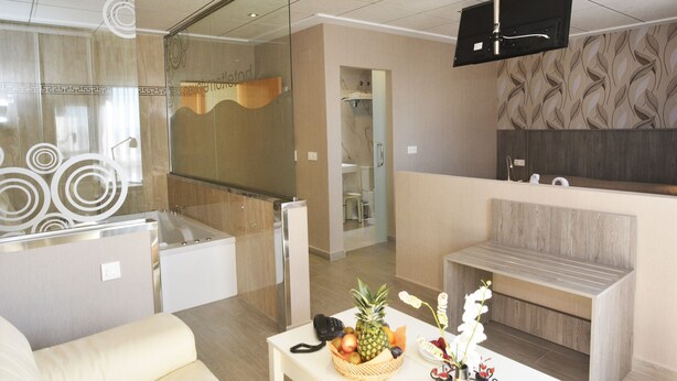 A modern hotel lobby with a reception desk, a seating area, a large mirror, and a television mounted on the ceiling. - Hotel Torrejoven (Torrevieja)