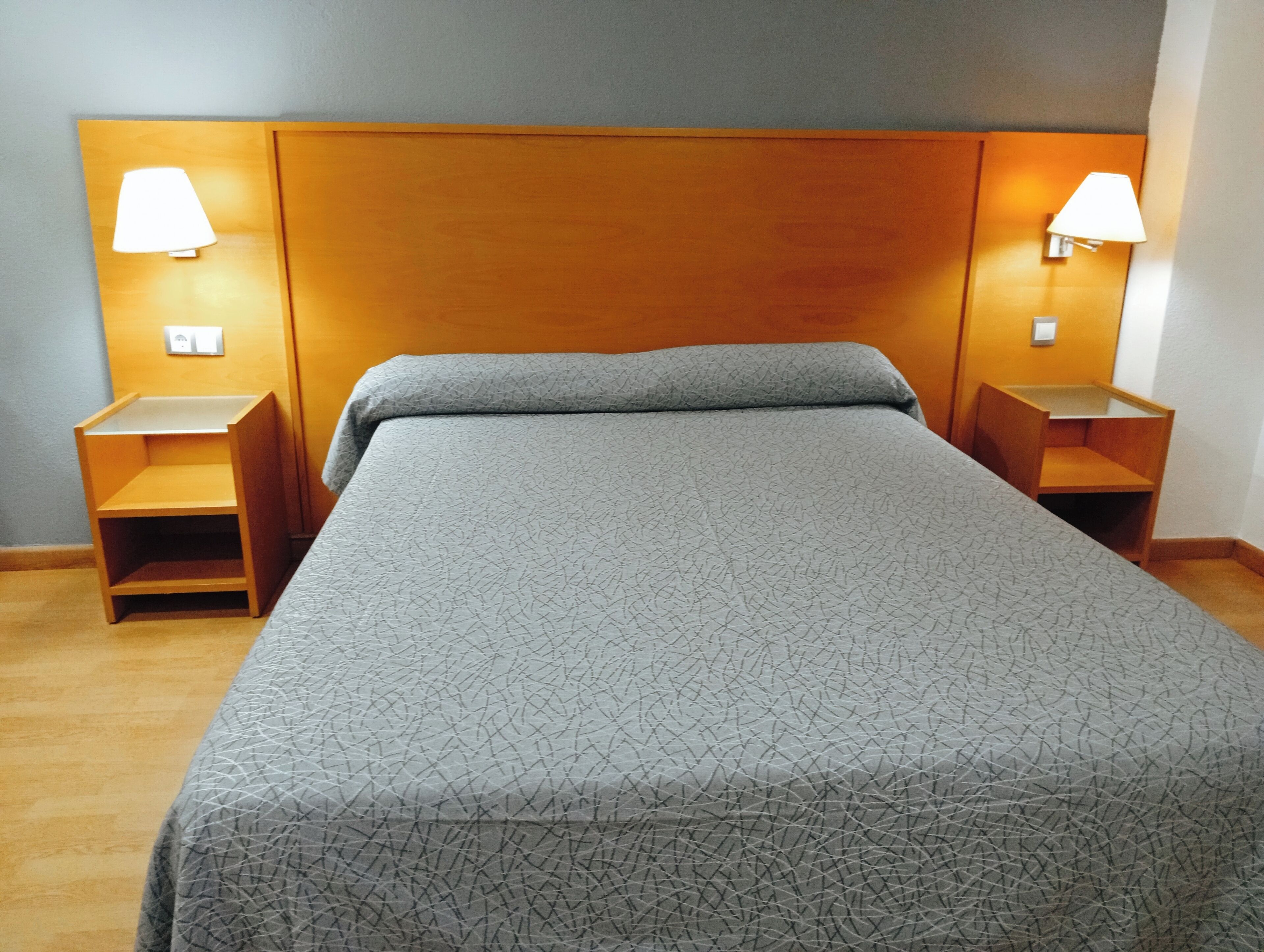 Ein Hotelzimmer mit einem großen Bett, einem hölzernen Kopfteil, zwei Nachttischen mit Lampen und einer kleinen Ablagefläche auf jeder Seite.
