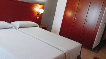 Una habitación de hotel con una cama grande, una mesita de noche con lámpara, un armario y una alfombra roja.
