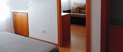 Habitación de hotel con una cama, un televisor fijado a la pared, una puerta de madera y vistas al área de estar.