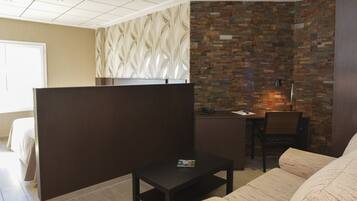 Una habitación de hotel moderna con sofá modular, una mesita, un escritorio con silla y una pared decorativa con diseño de hojas.
