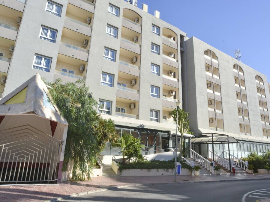 A multi-story hotel with balconies, a gated entrance, and a covered outdoor area with stairs.
