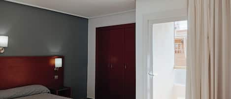 A hotel room with a bed, a wardrobe, a nightstand, and a door leading to a balcony.