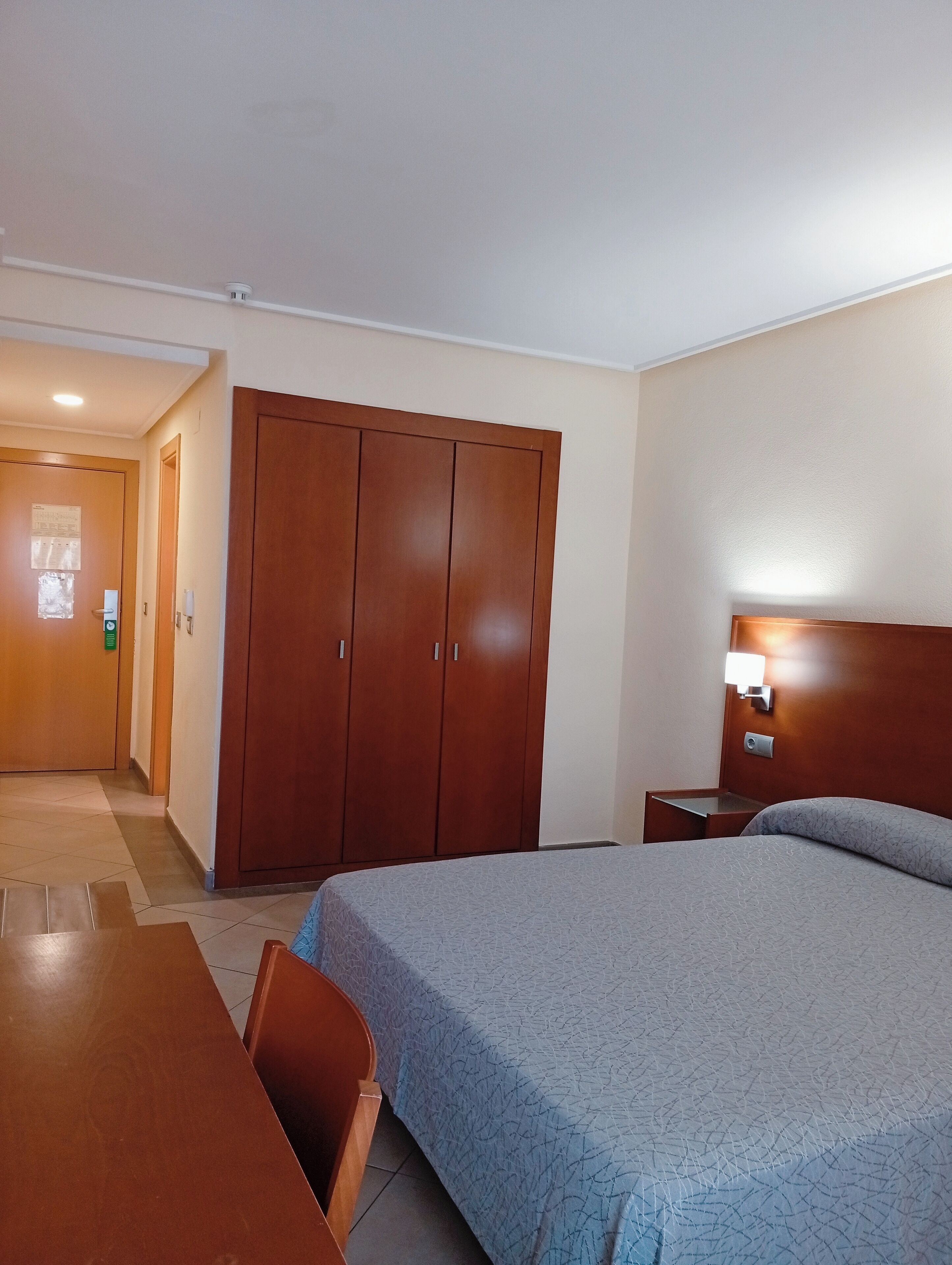 Una habitación de hotel con cama, armario de madera, escritorio y mesita de noche.