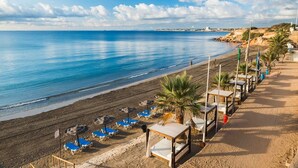 A beach with sun loungers and umbrellas, a sandy walkway, and a view of the sea. - Hotel Torrejoven (Torrevieja)