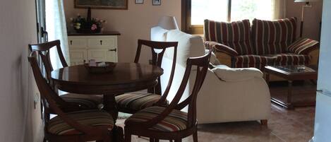 Un comedor con una mesa y sillas de madera, un sofá y un ventanal con cortinas.