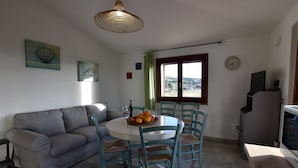 Ein Essbereich mit einem runden Tisch, vier Stühlen, einer Couch und einem Fenster mit Vorhängen.