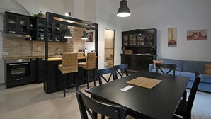Una cucina moderna con mobili scuri, un'area pranzo con tavolo e sedie nere e un divano blu nella zona soggiorno.