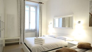 Una camera da letto con un letto, un comodino, una finestra con tende, un termosifone, un armadio e uno specchio a parete.