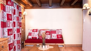Une pièce chaleureuse avec un banc en bois, une petite table ornée de bougies et un mur décoré d’une courtepointe aux motifs rouges et blancs.
