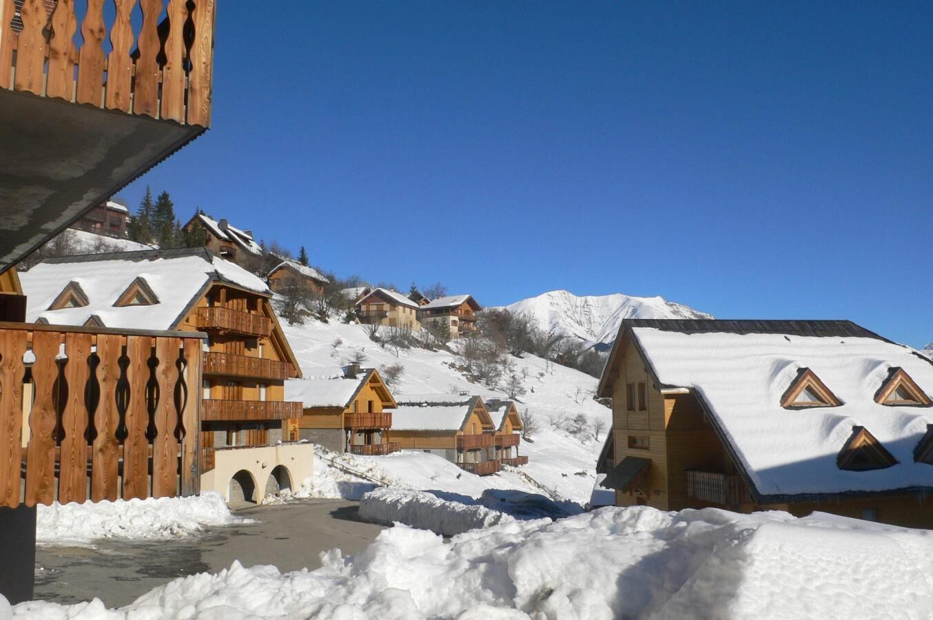 A snow-covered village with wooden houses, a wooden fence, and a clear blue sky.