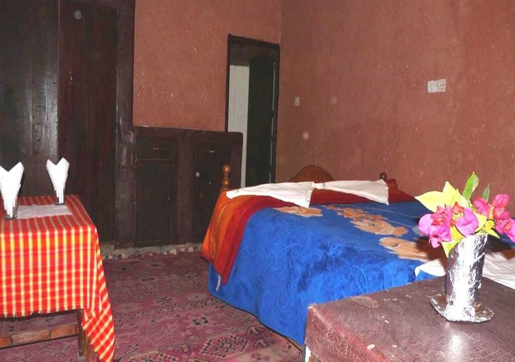A room with a bed, a table with a checkered tablecloth, and a vase with flowers.
