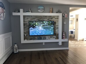 Una sala de estar con televisor, chimenea de piedra y adornos en estanterías.
