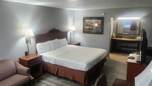 Habitación de hotel con cama, escritorio, silla, sofá, televisión y un cuadro en la pared.