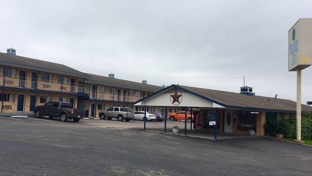 Un motel con un amplio estacionamiento, una zona techada con un emblema de estrella y un cartel.