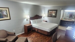 Un dormitorio con cama, mesitas de noche, una silla, una mesa y un espejo.