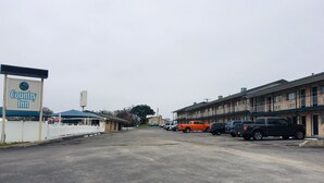 Una posada campestre con un letrero, un estacionamiento con varios coches y una hilera de edificios de varios pisos con balcones.