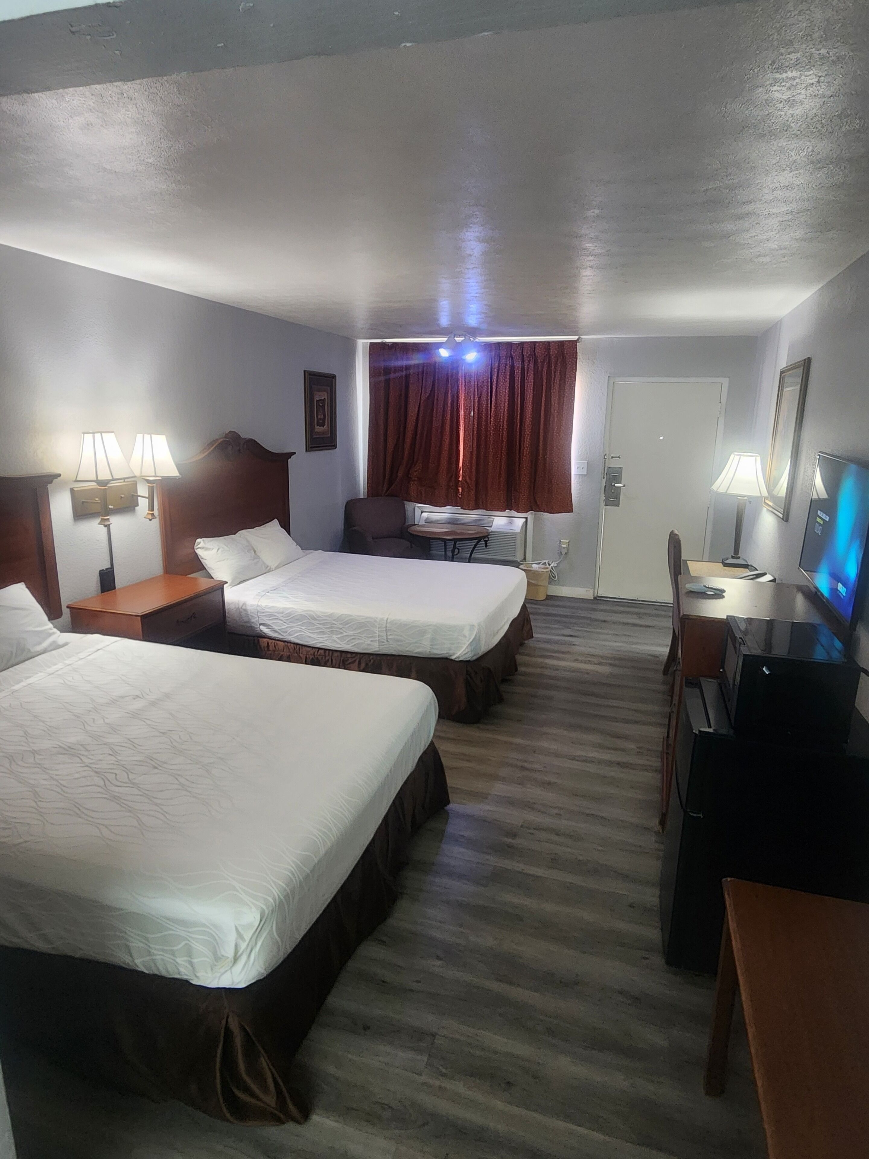 Habitación de hotel con dos camas, un escritorio, una silla, un televisor y una ventana con cortinas.