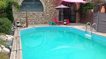 Relax by the pool surrounded by a patio area with a stone wall and arched window.