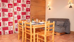 A dining area with a wooden table and chairs, a grey sofa, and a patterned curtain.